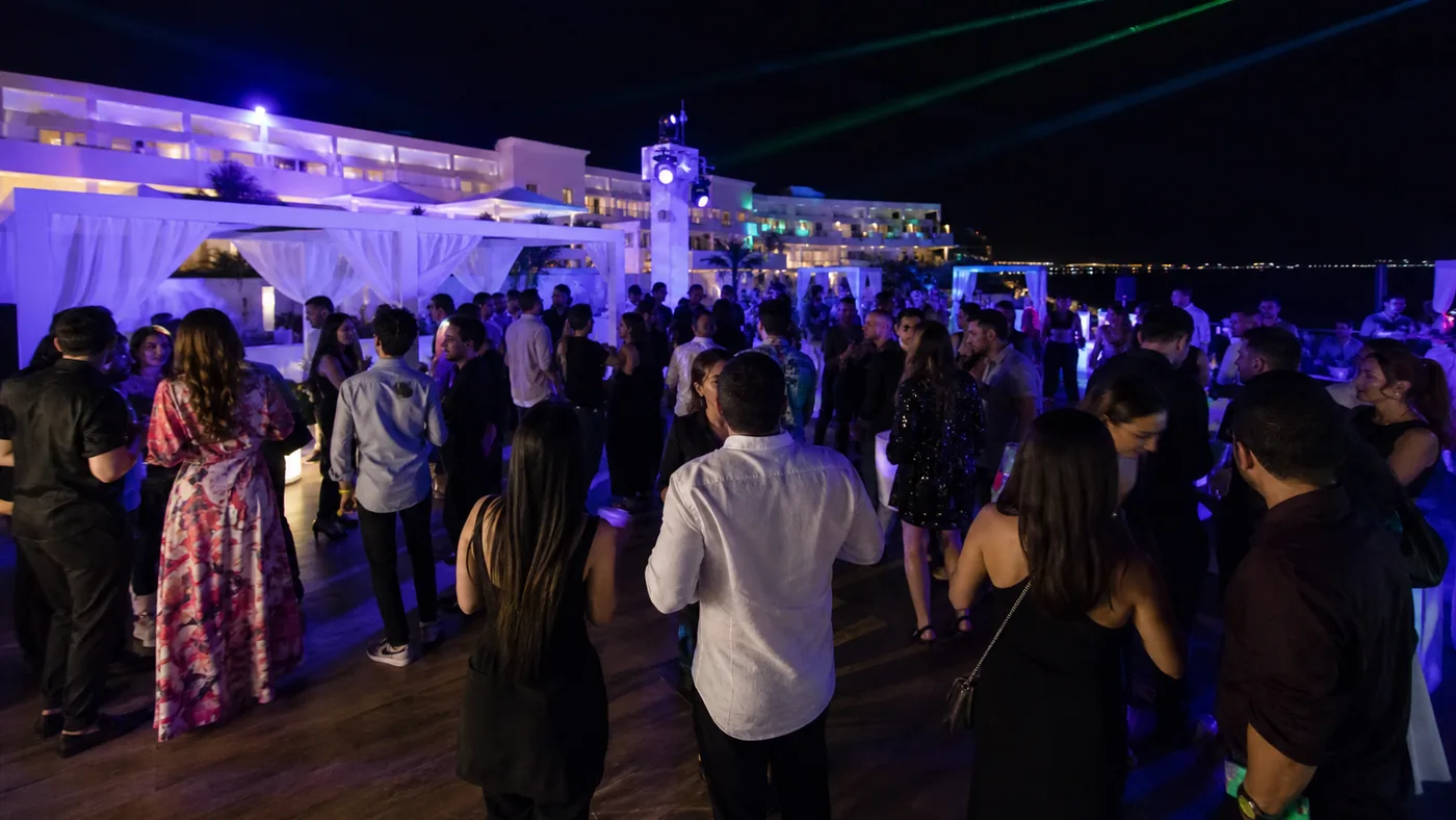 Fiesta nocturna de adultos en una terraza de resort iluminada en azul y violeta